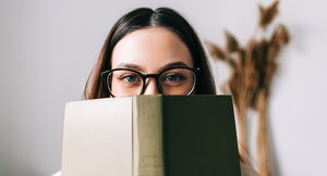 Frau mit Brille hält sich ein grünes Buch vor das Gesicht