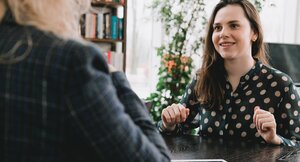 Junge Frau sitzt an einem Holztisch während eines Bewerbungsgespräches