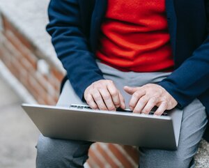 Mann mit rotem Pullover und blauer Jacke arbeitet am Laptop