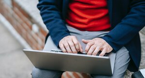 Mann mit rotem Pullover und blauer Jacke arbeitet am Laptop