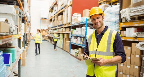 Aus- und Weiterbildungen für Transportwesen, Lager und Logistik Lagerarbeiter hält Clipboard in der Hand und lächelt in die Kamera